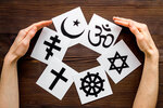 Hände umarmen das Christentum, den Katholizismus, den Buddhismus, den Judentum, Islam-Symbole auf Holzhintergrund