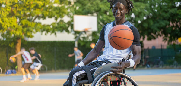 Mann mit Behinderung im Rollstuhl auf einem Basketballplatz